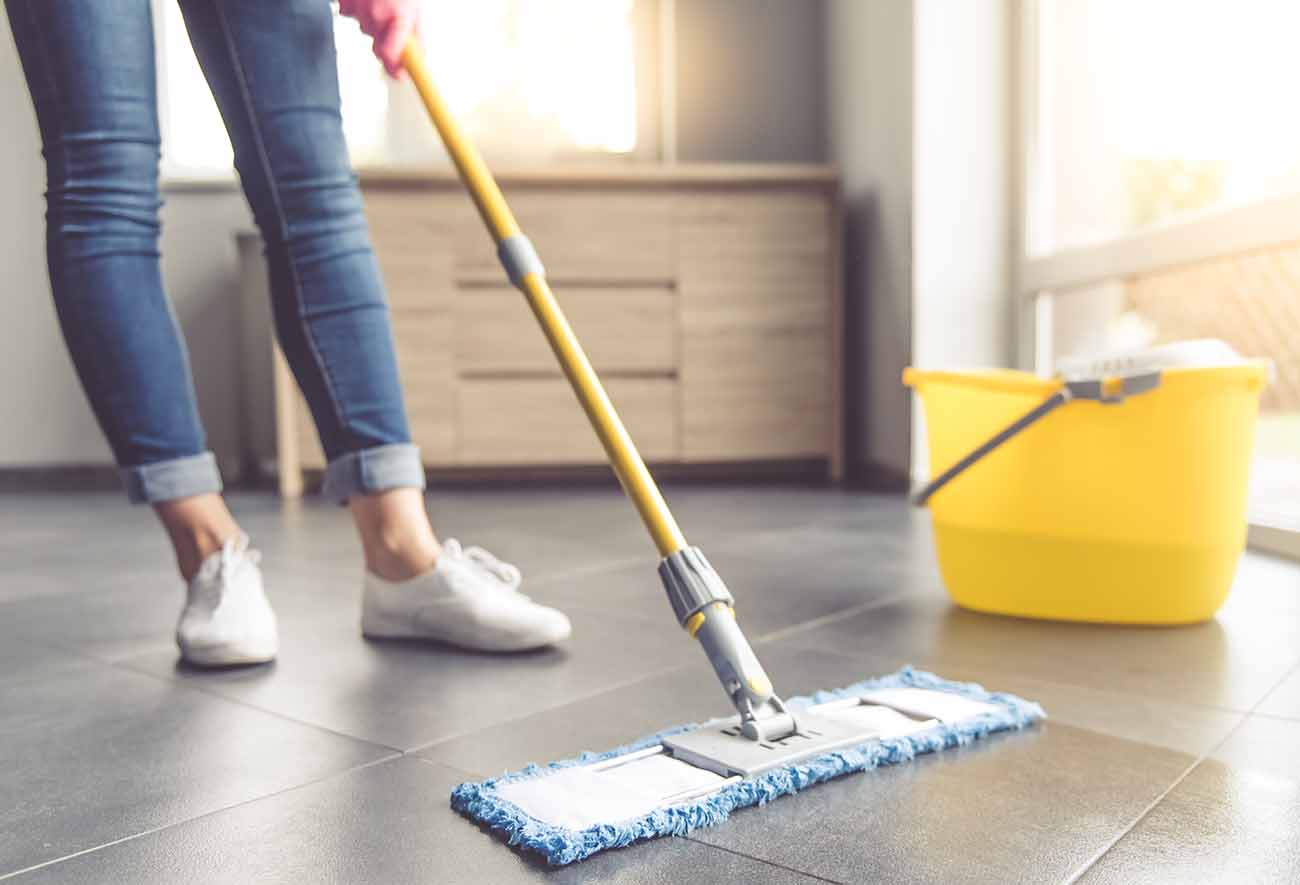Imagem cortada de uma mulher com luvas de proteção usando um esfregão molhado plano durante a limpeza do chão na casa